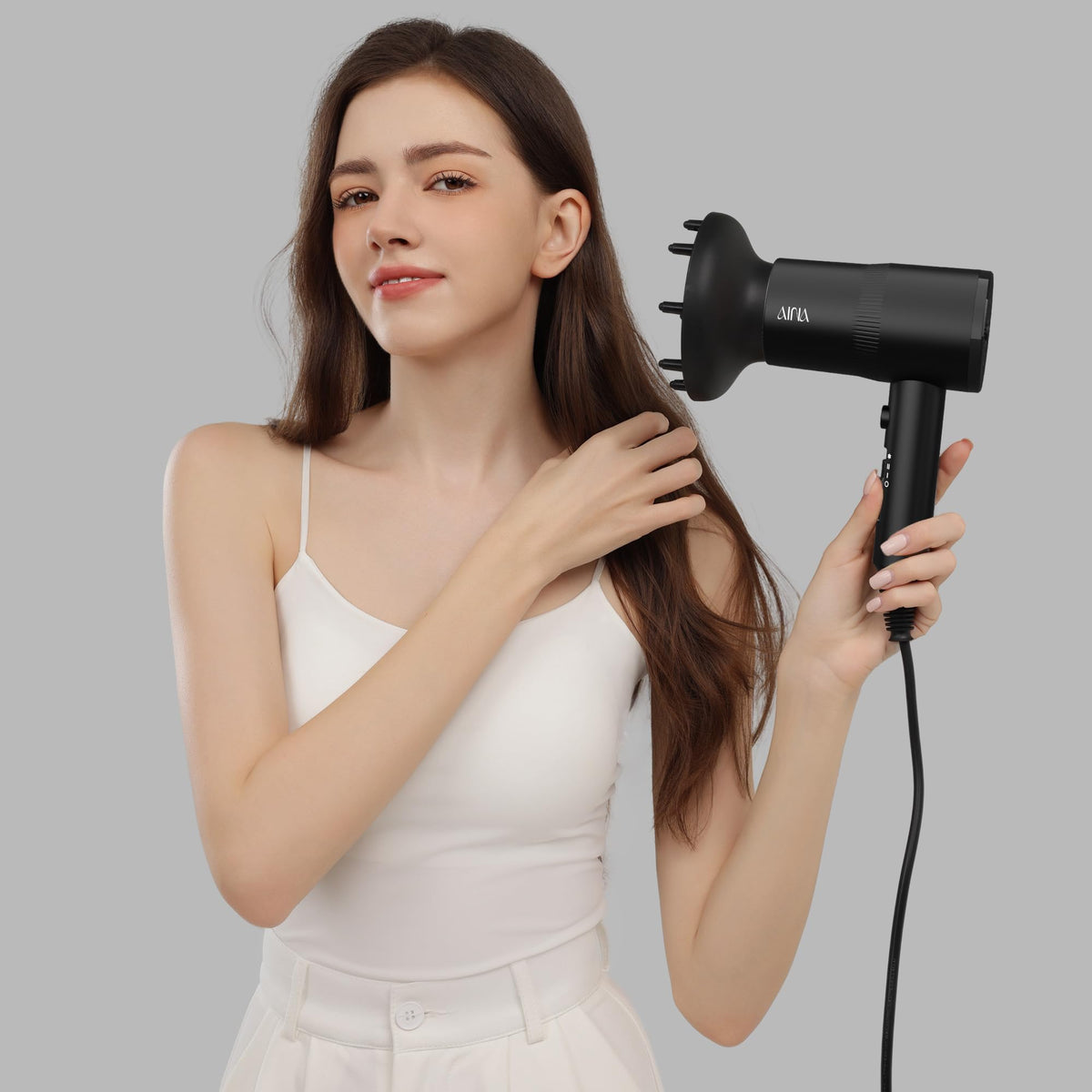 AINA dryer held beside hand to show compact size and travel-friendly portability