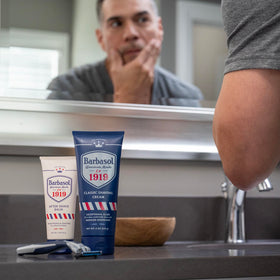 Barbasol 1919 on a bathroom shelf with grooming items, suggesting daily post-shave routine