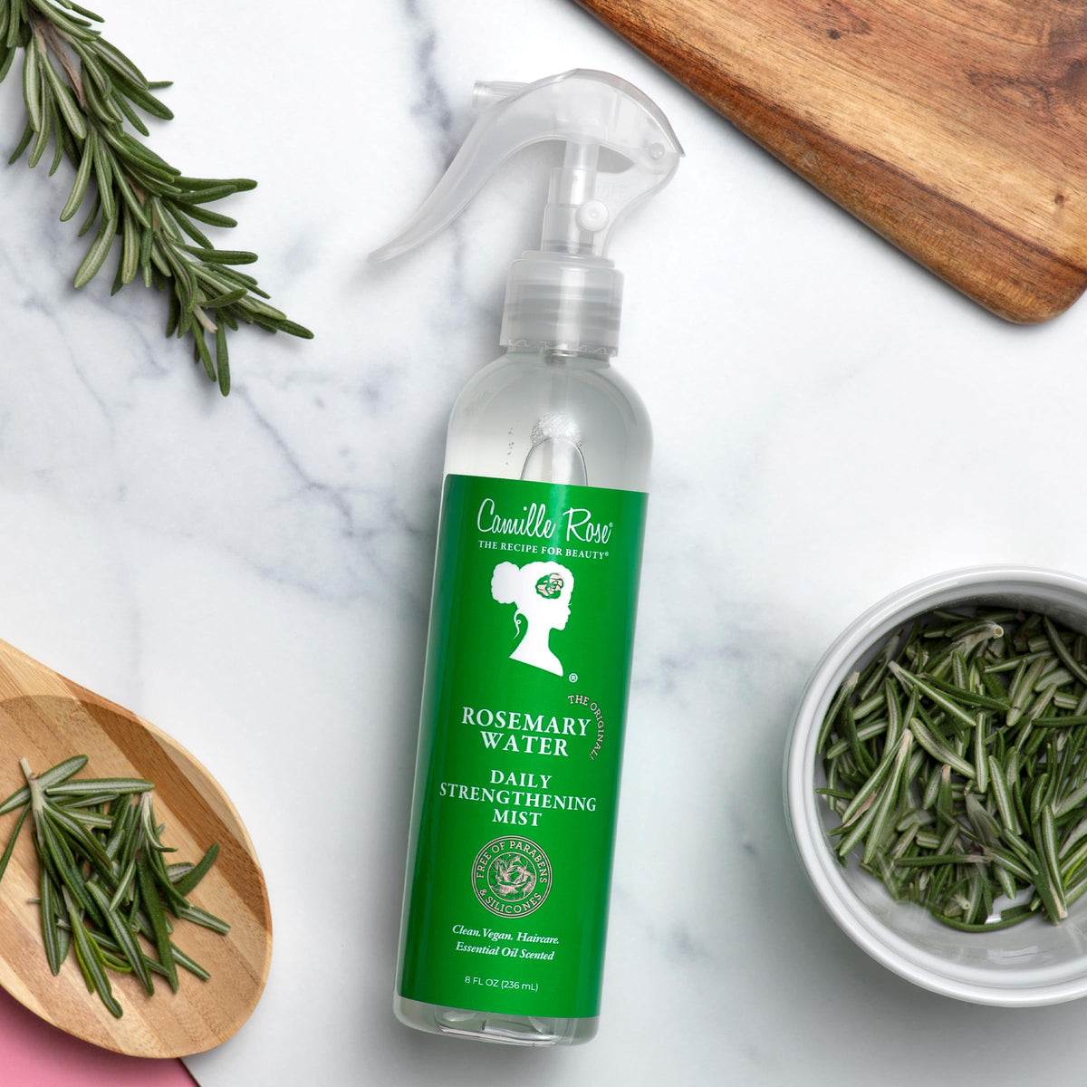 Camille Rose bottle beside fresh rosemary sprig highlighting natural botanicals