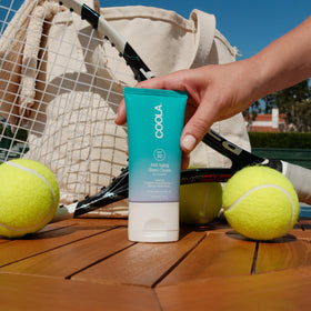 COOLA tube beside a smartphone illustrating compact 2 fl oz size