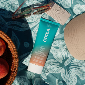 COOLA bottle on a beach towel lifestyle scene depicting reliable outdoor sun protection benefit