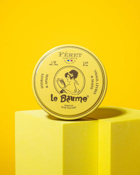 Feret Parfumeur tin among roses in a garden setting conveying powdery-rose scent benefit: subtle fragrance