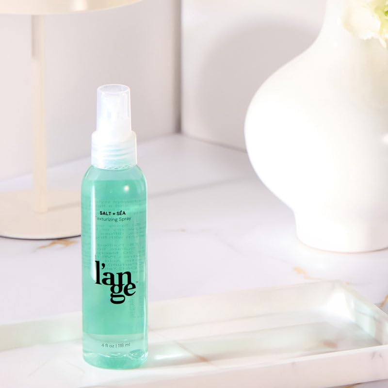 L'ANGE HAIR bottle beside hand to show compact 4 oz travel-friendly size