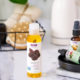 NOW Foods jojoba oil next to hand showing 4-ounce scale for travel-friendly convenience