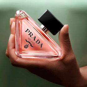 Prada Paradoxe fragrance pouring shot with liquid curve showing texture and luminous amber notes