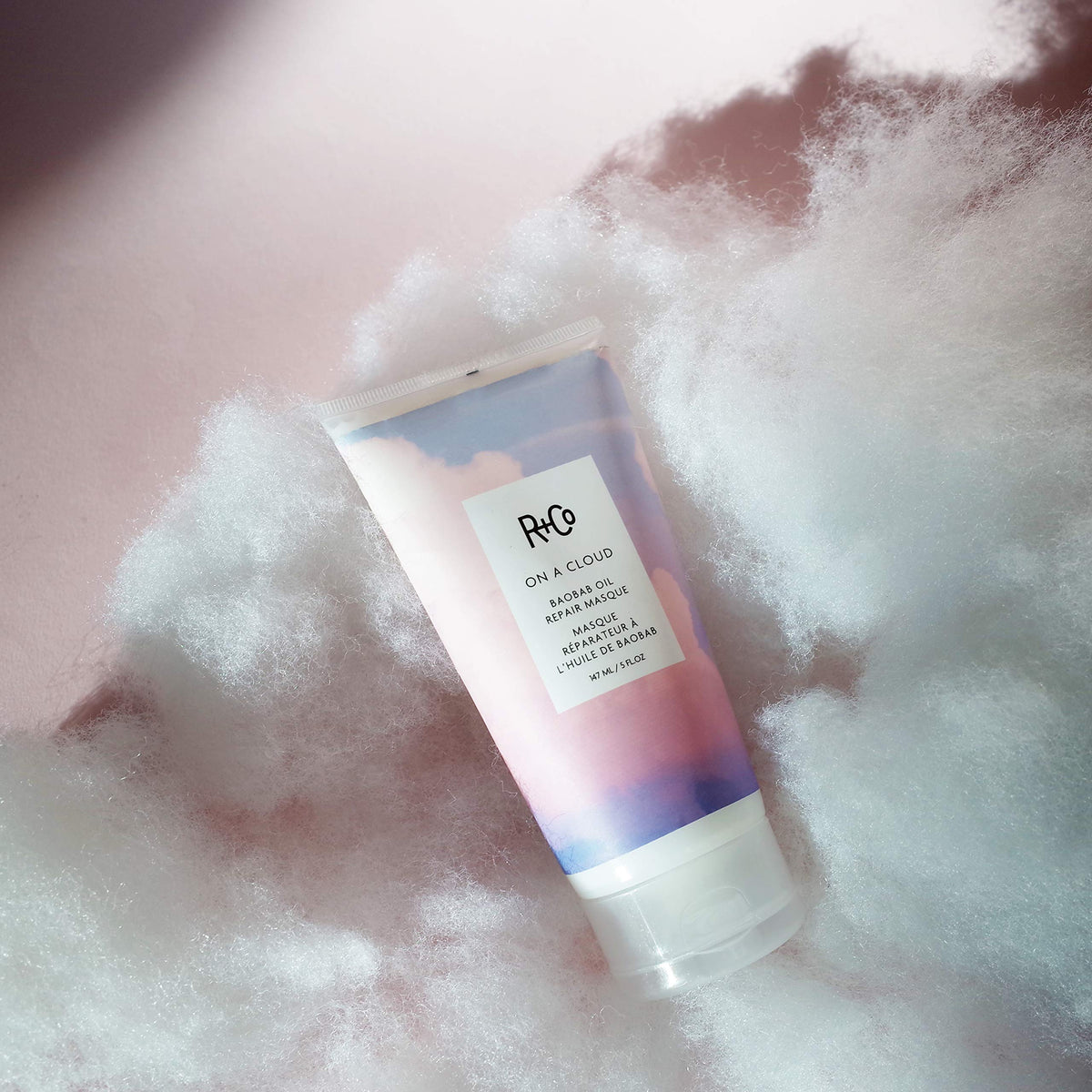 R+Co On A Cloud held in hand for scale showing compact 147 ml size ideal for home treatments