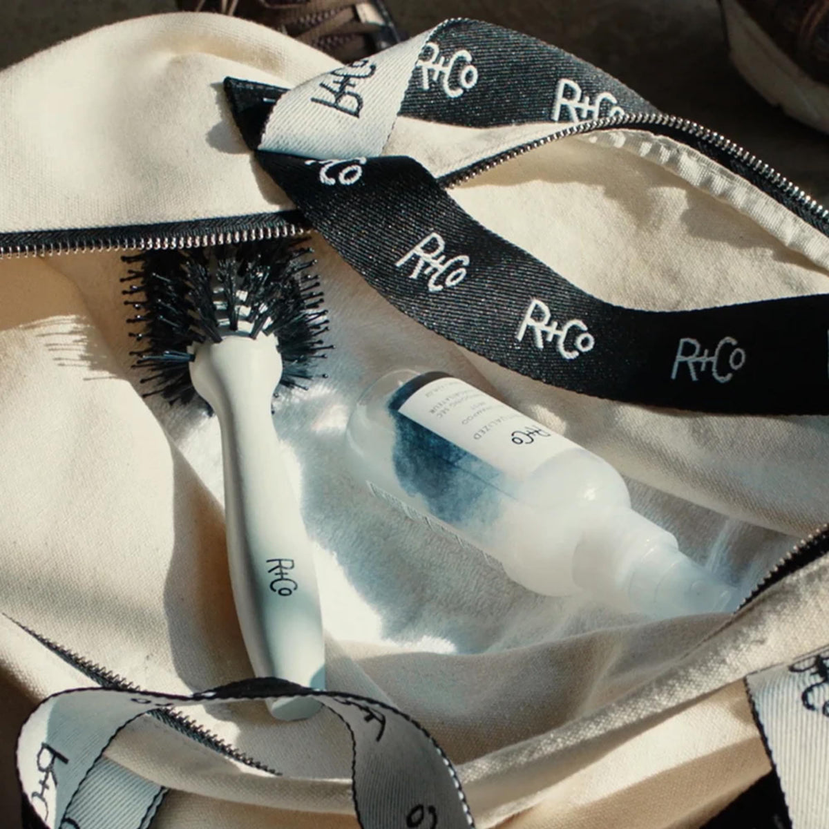 Hand holding R+Co Spiritualized bottle showing size and travel-friendly benefit