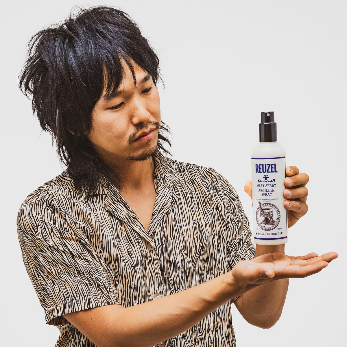 Reuzel bottle in hand showing 3.38 oz scale and travel-friendly benefit
