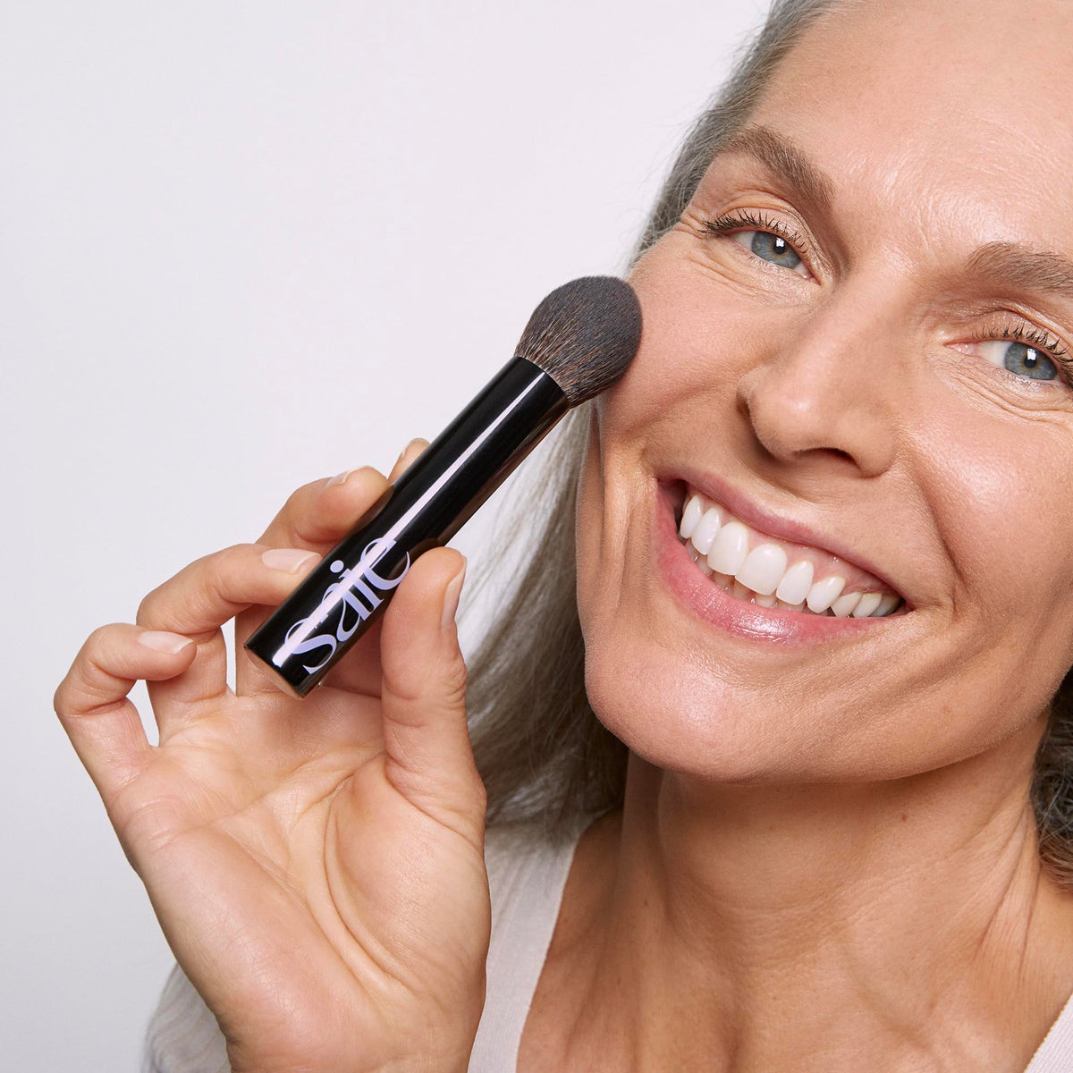 Saie Fluffy Brush applying loose powder to cheek for diffused finish