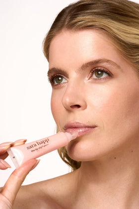 Sara Happ gloss held in hand to show compact 0.5 oz size and travel-friendly benefit