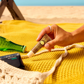 Sun Bum lip balm on beach towel lifestyle shot showing outdoor readiness