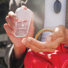 Touchland bottle held in hand showing 1 fl oz size and easy carry benefit