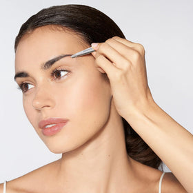Tweezerman mini slant held in hand to show scale and ergonomic control for travel and touch-ups