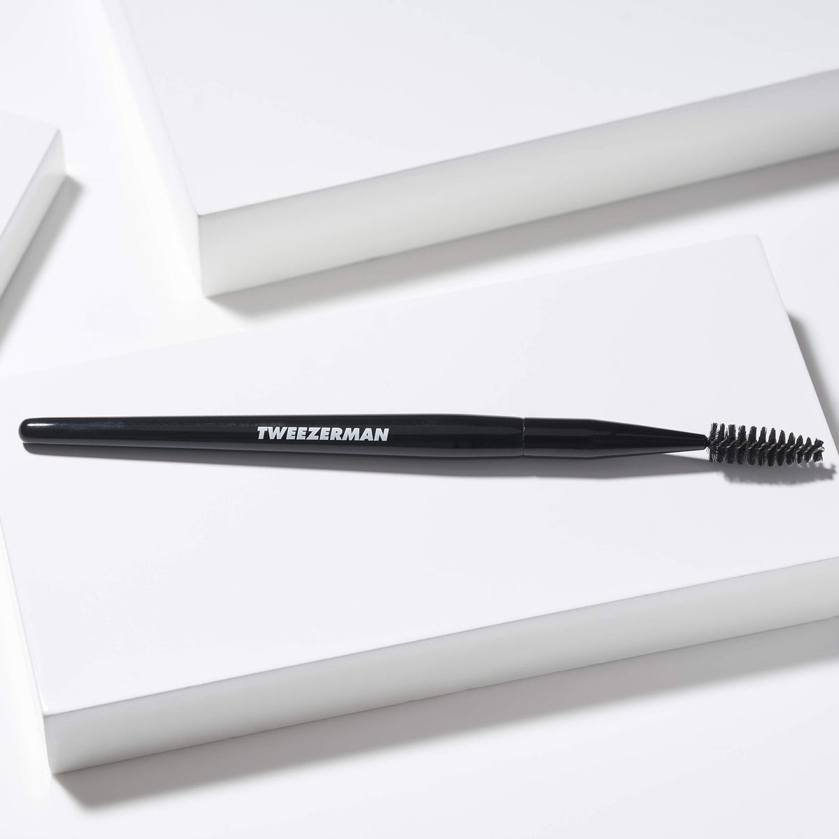 Tweezerman spoolie held in hand for scale and easy travel convenience